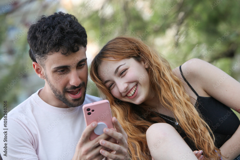 young cheerful couple using cellphone in the park on summer day young cheerful couple using cellphone in the park on summer day