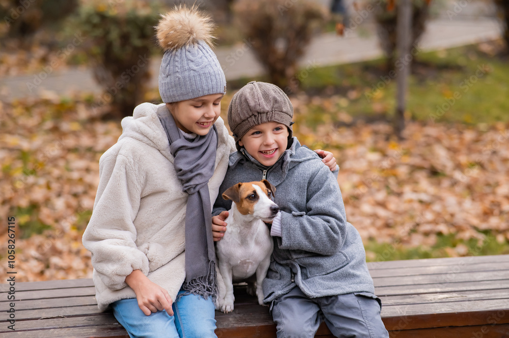 Brother and sister sit in an embrace with a dog on a bench for a walk in the autumn park. Boy, girl and jack russell terrier. Brother and sister sit in an embrace with a dog on a bench for a walk in the autumn park. Boy, girl and jack russell terrier.