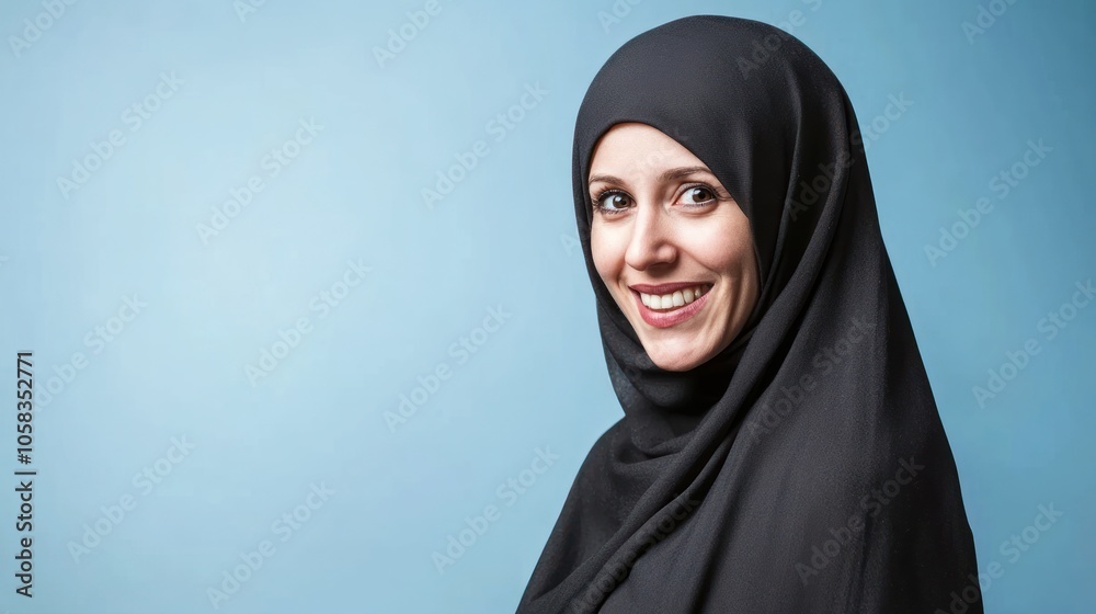 A smiling woman wearing a black hijab against a blue background. A smiling woman wearing a black hijab against a blue background.