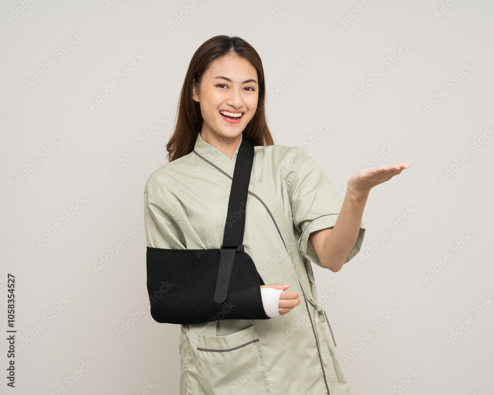 Happy young asian woman broken arm pointing finger on isolated background. Female put on plaster bandage cast splint. Patient wearing sling arm after accident injury. life insurance and accident