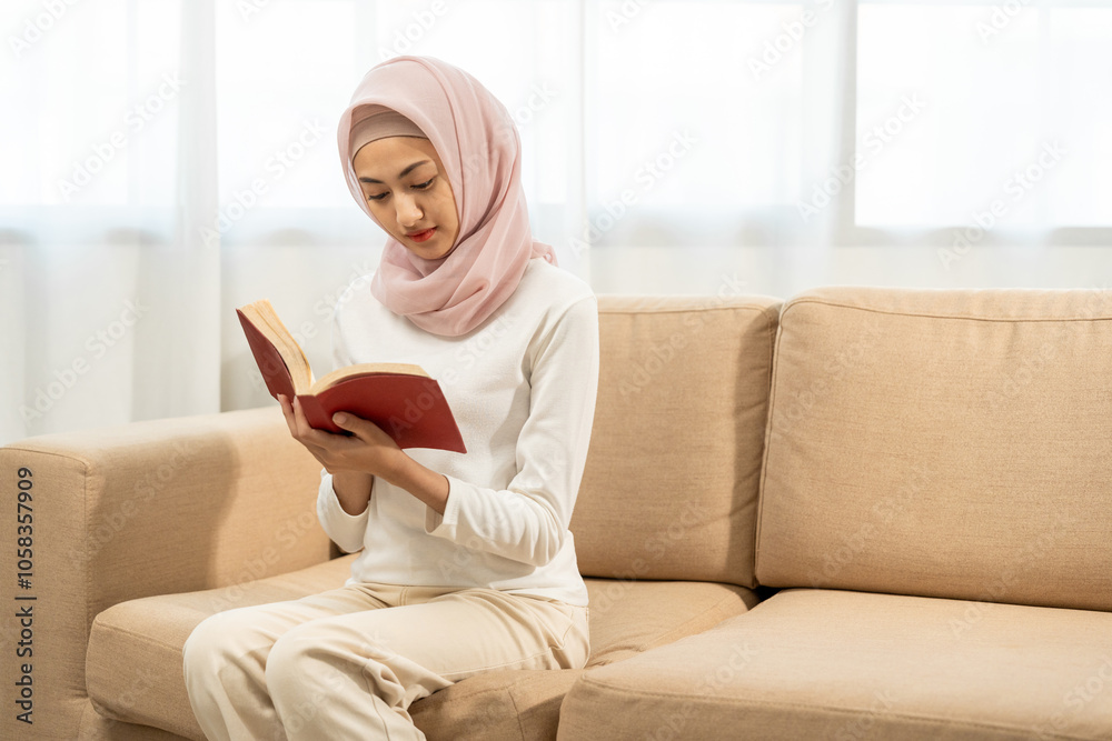 Portrait happy young asian muslim woman sitting on sofa in living room reading book. Beautiful Attractive Muslim woman wearing abaya and hijab costume in the house holding book
