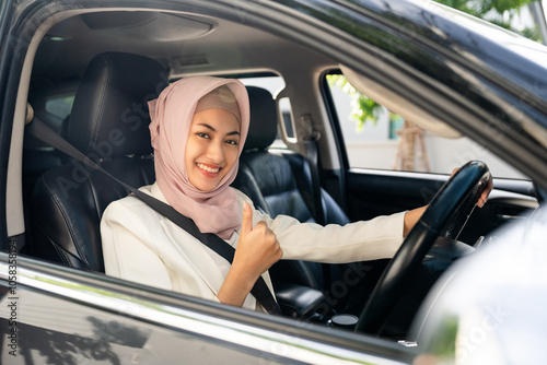 Asian muslim business women getting new car. She very happy and excited. Smiling female islamic driving vehicle on the road on a bright day with sun light. Business woman buying driving new car