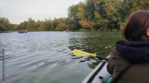 A woman sitting in a boat on a river and looking at other boats with people passing by on a cloudy autumn day. Kayaking tourism travel photo