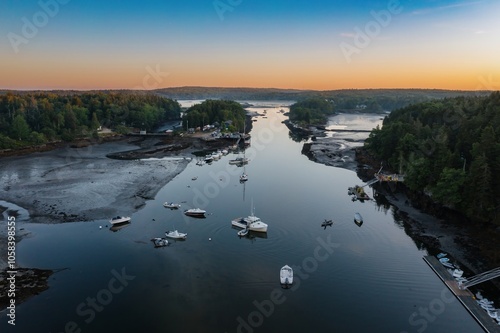 Boats moored in the calm Branch estuary during low tide at sunrise. The estuary is surrounded by forest, Phippsburg, Maine, United States. photo