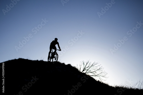 A man rides a bicycle down the mountain. Photo against the sun, silhouette against a blue sky.