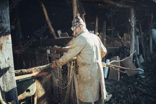 Man in trench coat and protective goggles cutting firewood on a photo