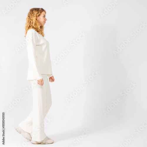 Young attractive blonde girl walking on white background, full-length portrait, copy space