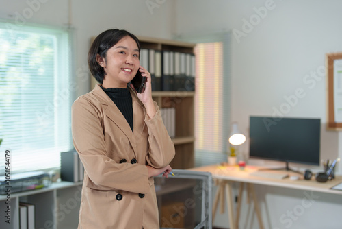 Attractive Asian businesswoman standing on the phone talking about real estate projects and chatting with happy smiles at the office.