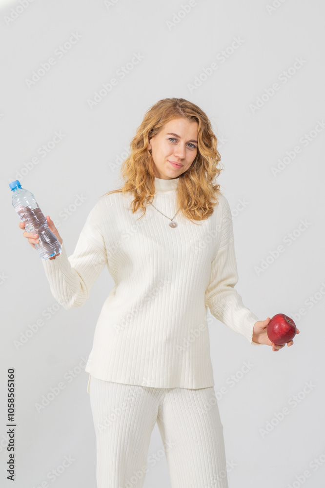 Happy young blonde girl holding a pure water bottle and an apple, white background, copy space