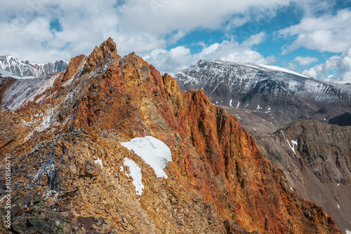 Vivid sharp pinnacle in sunlight. Shiny pointy peak of gold color. Colorful red rocky peaked top. Freshly fallen snow in high mountains. Sunny cloudy alpine view. Snowy cornice on stony mountain ridge photo