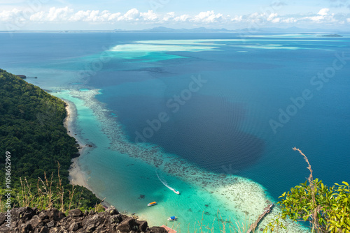 Spectacular view from above showcasing vibrant turquoise waters meeting a lush green coastline, dotted with boats, under a clear blue sky.