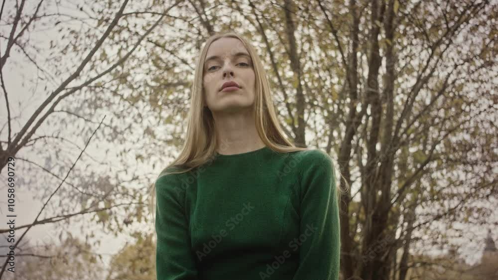 Woman with long blond hair poses gracefully in an autumn park, dressed in a stylish green sweater. The serene setting features vibrant leaves and soft, golden light Woman with long blond hair poses gracefully in an autumn park, dressed in a stylish green sweater. The serene setting features vibrant leaves and soft, golden light