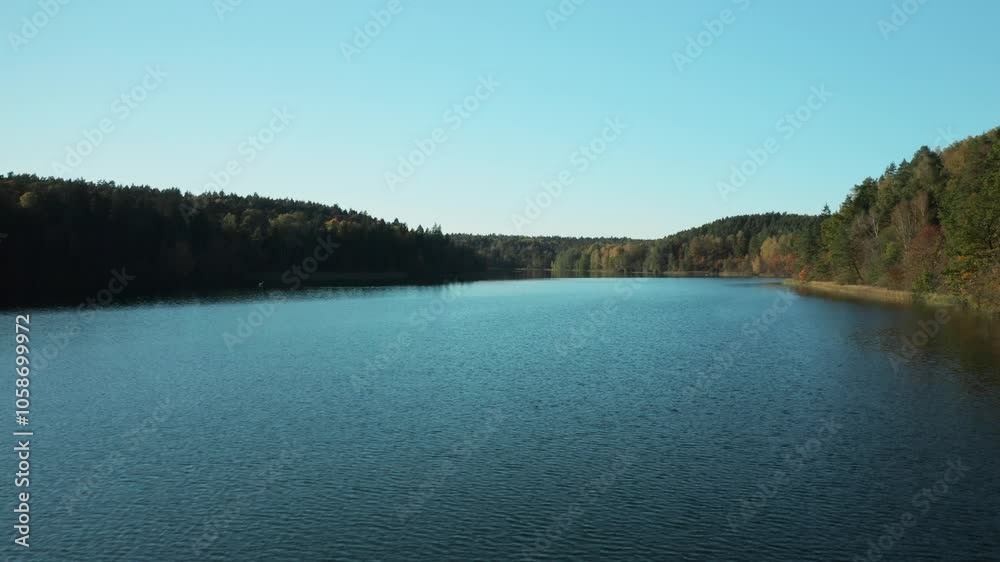 AERIAL: Birds eye view of scenic emerald lake surrounded by forest in autumn