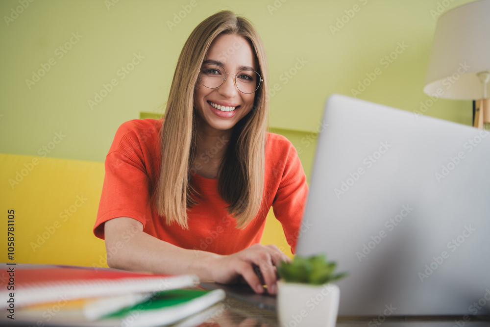 Photo of lovely young girl working netbook dressed orange garment spacious house spring indoors room Photo of lovely young girl working netbook dressed orange garment spacious house spring indoors room