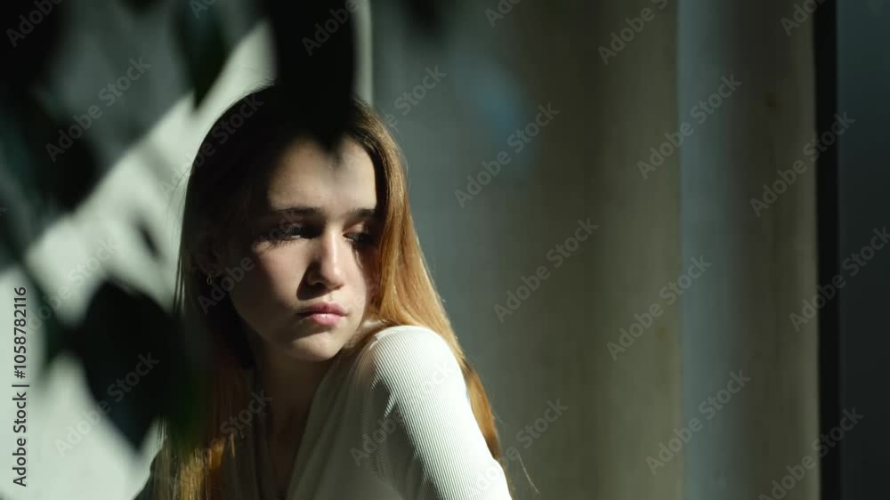 Sad young girl, teenager sitting at a cafe table in the rays of the bright summer sun