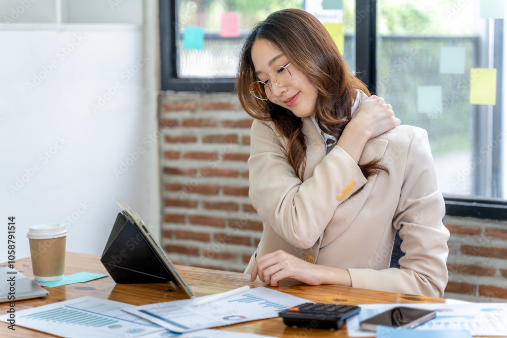 Tired young businesswoman using one hand to massage her shoulder to ease the neck and shoulder pain from long working hours Tired young businesswoman using one hand to massage her shoulder to ease the neck and shoulder pain from long working hours