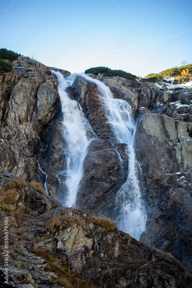 Obraz premium The Wielka Siklawa waterfall in the Valley of Five Ponds, Tatra Mountains, Zakopane, Poland, cascades dramatically over rocky cliffs, creating a mesmerizing scene in this alpine landscape.