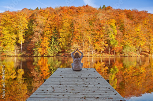 Woman meditating outdoors in the autumn park near forest lake.