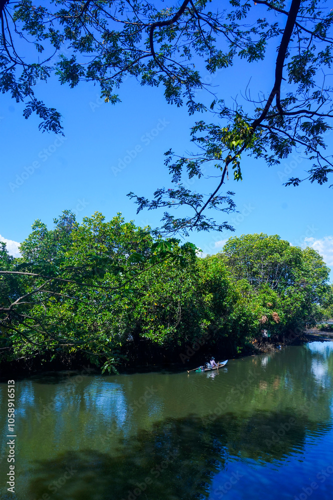 view of a fisherman driving a boat on a river with a backdrop of trees and blue sky view of a fisherman driving a boat on a river with a backdrop of trees and blue sky