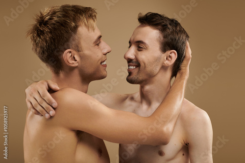 A joyful young couple shares a loving embrace, smiling at each other in soft light.