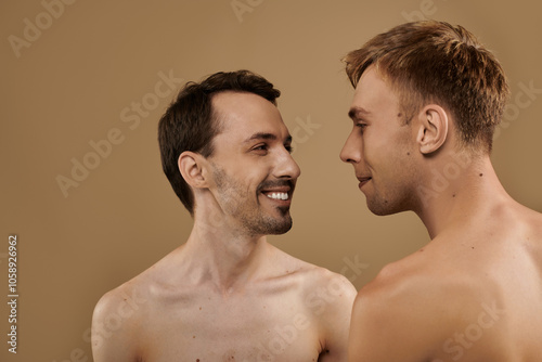 Two young men gaze into each others eyes, sharing joyful smiles in a cozy setting.