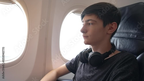 Teenager Wearing Headphones Sits Calmly in Airplane Cabin While Preparing for Takeoff on Exciting Journey. Young boy is seated in plane cabin, wearing headphones