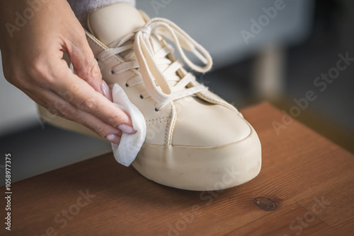 Person cleaning beige sneakers with cloth on table