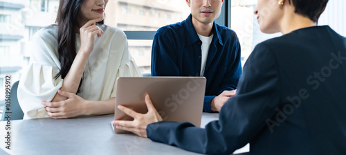 説明をするスーツを着た女性と話を聞くカップル photo