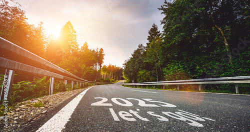 New year 2025 or start straight and beginning concept. Man ride on bike and the number 2025 start written on the road at sunset with lens flare. Concept of challenge or career path, business strategy. photo