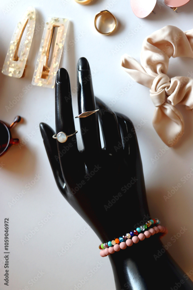 Hand figurine, sunglasses, gold jewelry, colorful bead jewelry, statement rings and various hair accessories on the white table. Flat lay.