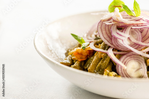 Loubieh Bzeit served in a ceramic dish topped with sliced red onions. photo