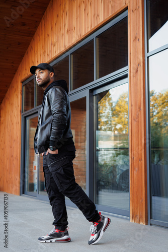 Full length of young african american man in leather jacket walking near building on street