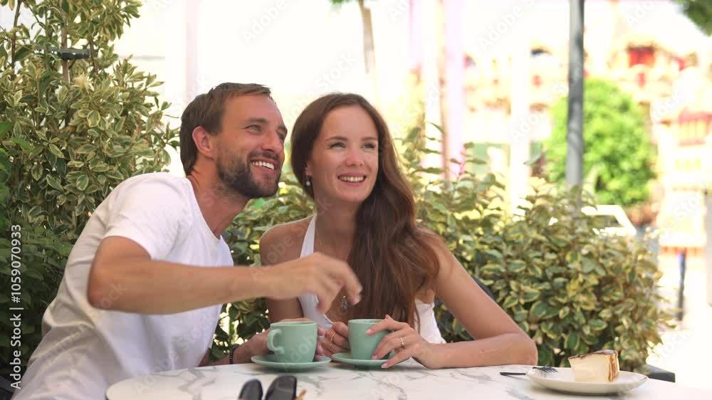 A young couple sits together in a stunning green setting, sipping coffee and sharing a slice of cheesecake while enjoying a lively conversation.