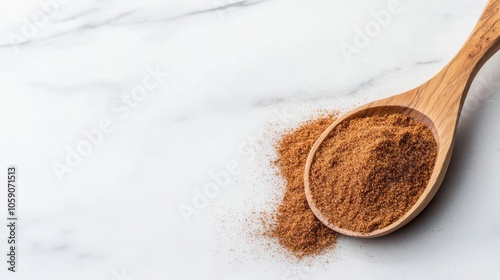 Brown spice in a wooden spoon on a marble surface, isolated view.