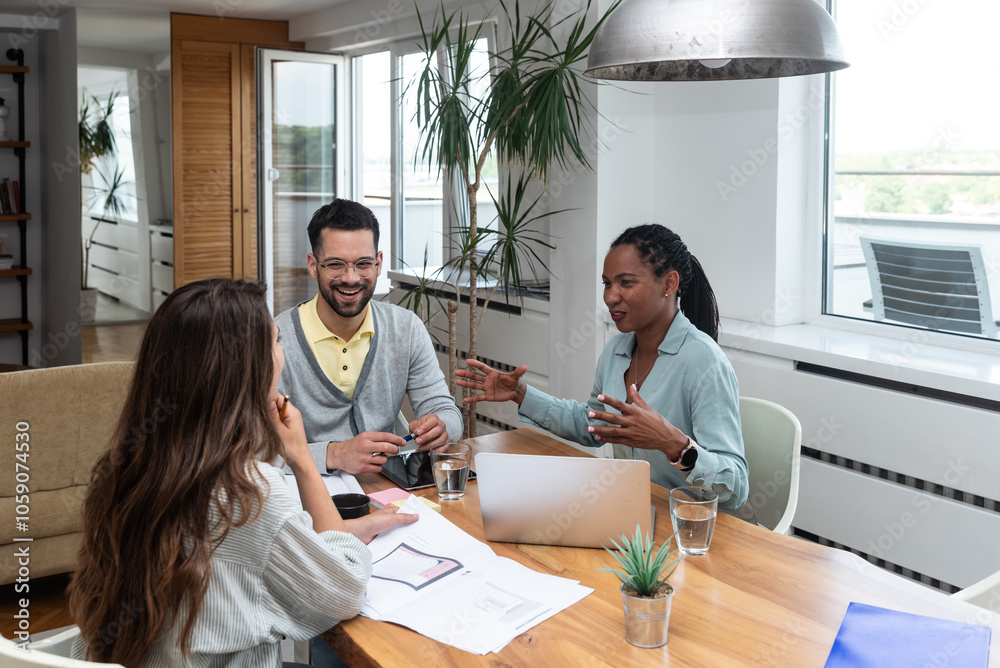 Obraz premium Diverse group of smiling young business people working together on a laptop during a meeting in modern small office. Businessman and businesswoman work on new innovative project of cheap housing.