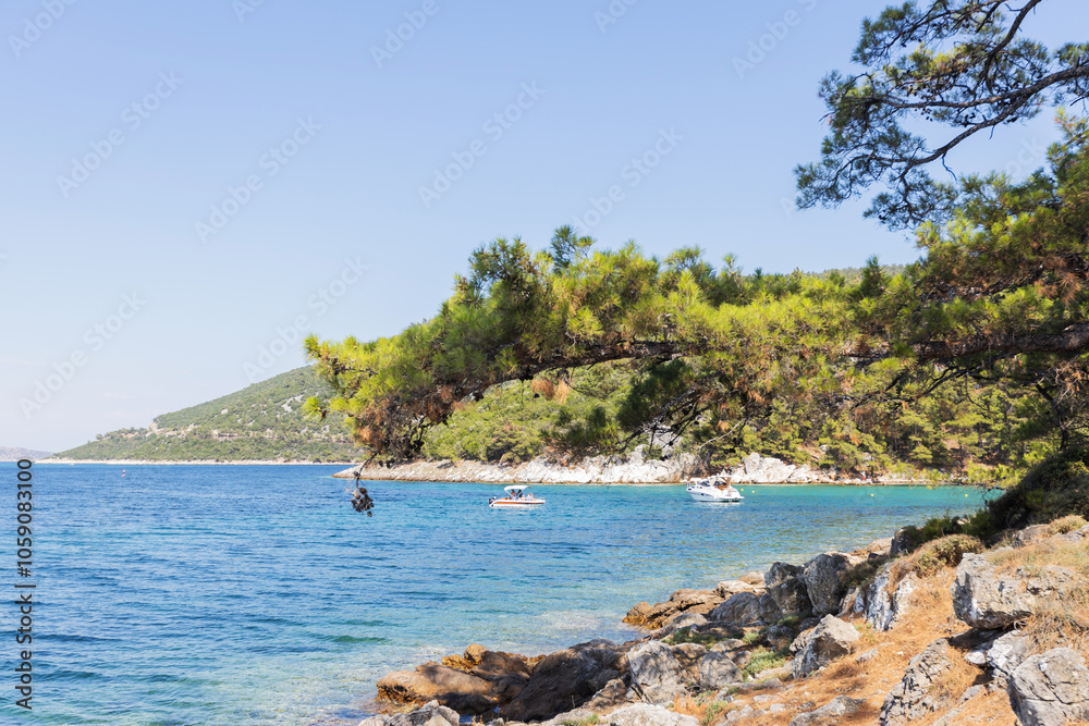 Obraz premium Boats near rocky shore surrounded by pine trees and clear blue waters