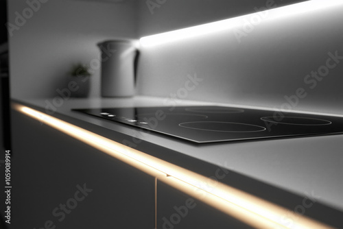Close-up of a modern induction cooktop on a minimalist kitchen countertop, highlighted by warm under-cabinet lighting that adds elegance and depth to the space
