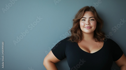 Confident plus-size woman in a black top smiling gently, standing against a neutral gray background, exuding self-assurance and positivity