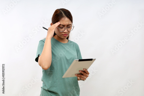 Attractive young asian woman holding a digital tablet while standing scratch her head over white background with confused face expression photo