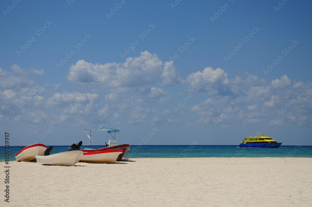 Fototapeta premium Beach scene: boats on shore, ferry in turquoise ocean under cloudy sky