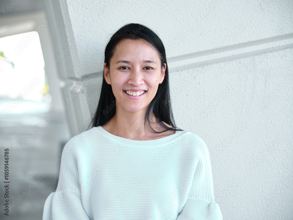 Smiling Asian woman standing in front of a blank wall outside