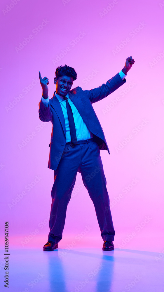Full-length portrait of happy young Indian man, businessman in formal wear dancing in joy against purple studio background in neon light. Concept of emotions, lifestyle, success, achievement Full-length portrait of happy young Indian man, businessman in formal wear dancing in joy against purple studio background in neon light. Concept of emotions, lifestyle, success, achievement