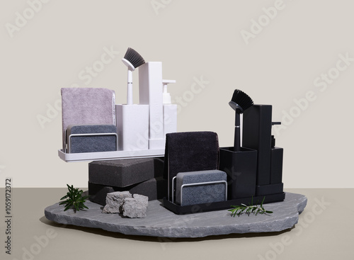 Black and white sink organisers sitting on top of a flat rock with rosemary sprigs on the side photo