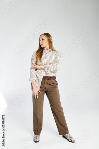 A woman with long hair stands poised in a striped shirt and pants, radiating confidence in a studio.