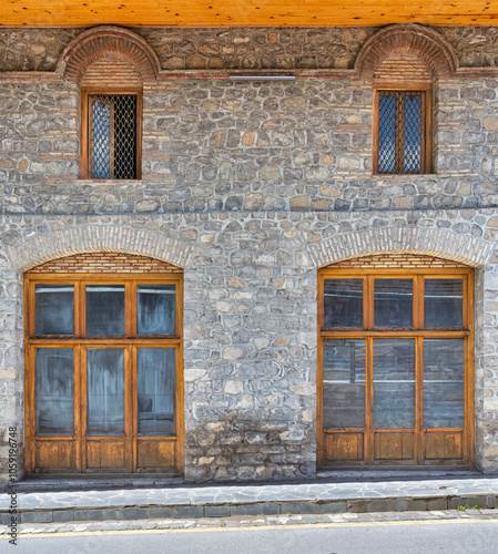 The rustic stone building features large wooden windows, highlighting the craftsmanship of old architecture in a tranquil village. The structure reflects a timeless charm