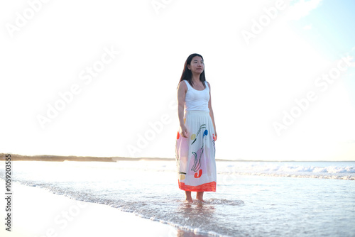 Asian woman wearing a long skirt walking along the beach photo