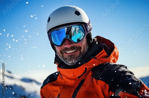 Portrait d'un homme au ski, âgé de 40 ans, souriant, portant une barbe, un casque de protection et des lunettes de soleil, ciel bleu magnifique en arrière-plan.