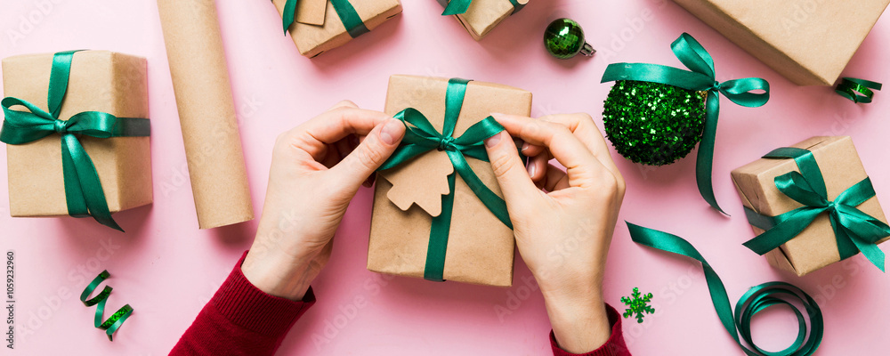 Fototapeta premium Woman is packing surprise gift for Christmas holidays, sitting at workplace with craft tools, top view. Woman wrapping Christmas gift at colored table