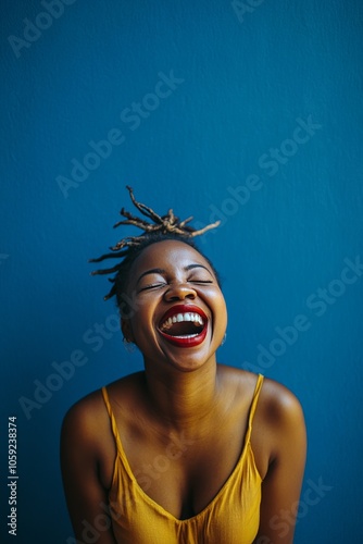 Young woman smiling with hand on her cheek against a blue wall in bright sunl...