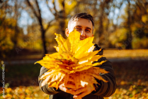 middle-aged man holding maple leaves in front of face in a park